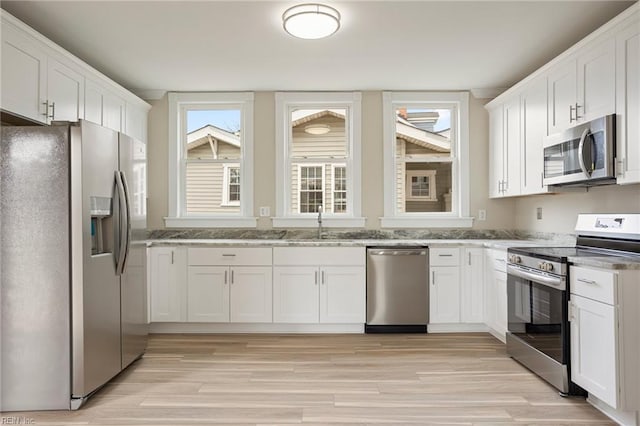 kitchen featuring appliances with stainless steel finishes, a sink, white cabinetry, and light wood-style floors