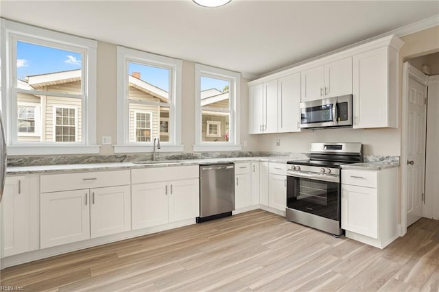 kitchen with stainless steel appliances, white cabinets, a sink, and light wood finished floors