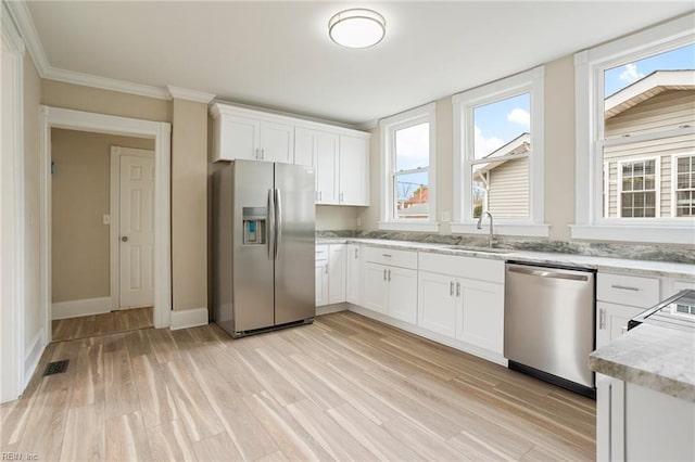 kitchen with light wood finished floors, appliances with stainless steel finishes, white cabinets, a sink, and light stone countertops