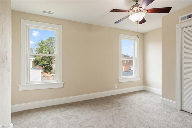 spare room with carpet floors, a wealth of natural light, visible vents, and baseboards