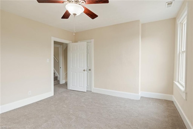 carpeted empty room featuring stairs, ceiling fan, visible vents, and baseboards