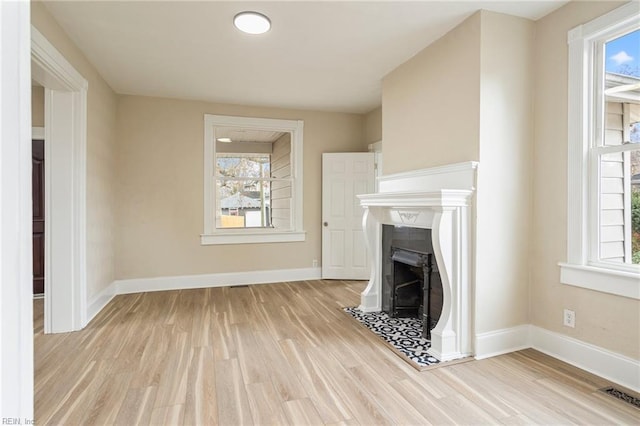 unfurnished living room featuring plenty of natural light, a fireplace with flush hearth, visible vents, and light wood-style floors