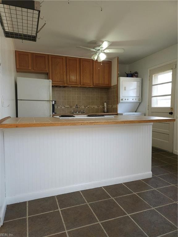 kitchen with brown cabinets, tasteful backsplash, tile counters, freestanding refrigerator, and stacked washer / dryer