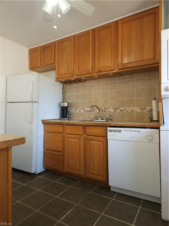 kitchen with brown cabinets, tasteful backsplash, a sink, white appliances, and dark tile patterned floors