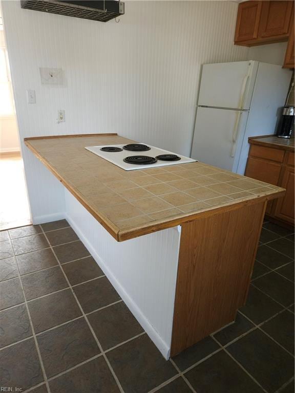 kitchen with dark tile patterned flooring, white appliances, tile countertops, and a kitchen bar