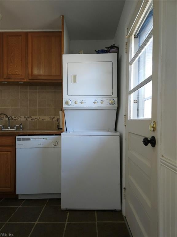 clothes washing area featuring laundry area, dark tile patterned floors, stacked washing maching and dryer, and a sink