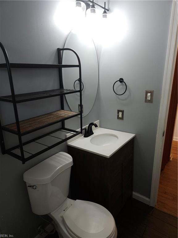 half bathroom featuring wood finished floors, vanity, toilet, and baseboards