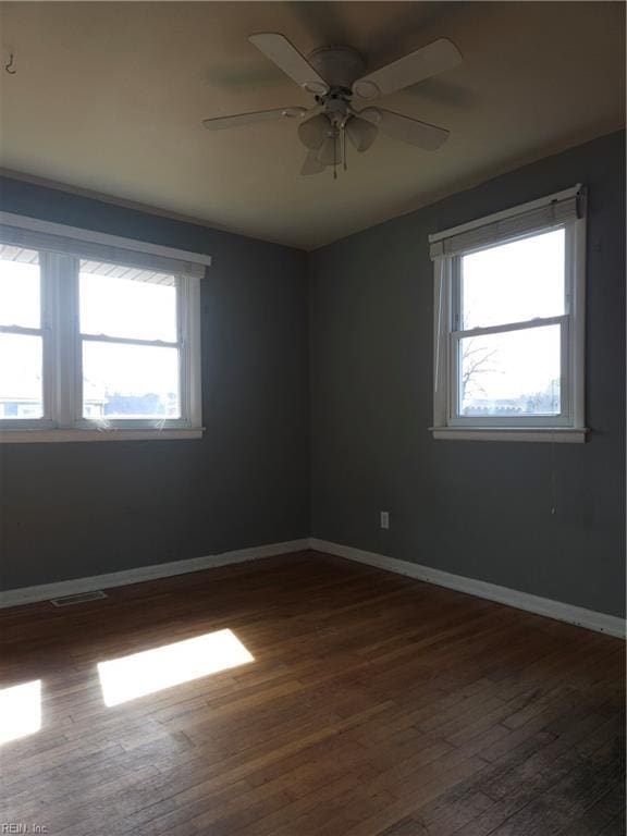 empty room with dark wood-style floors, baseboards, visible vents, and ceiling fan