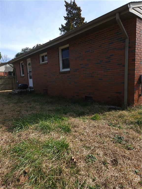 view of side of property with brick siding, a lawn, and fence