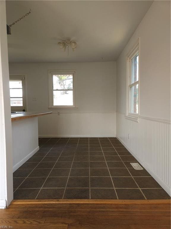 spare room featuring a wainscoted wall and dark tile patterned flooring