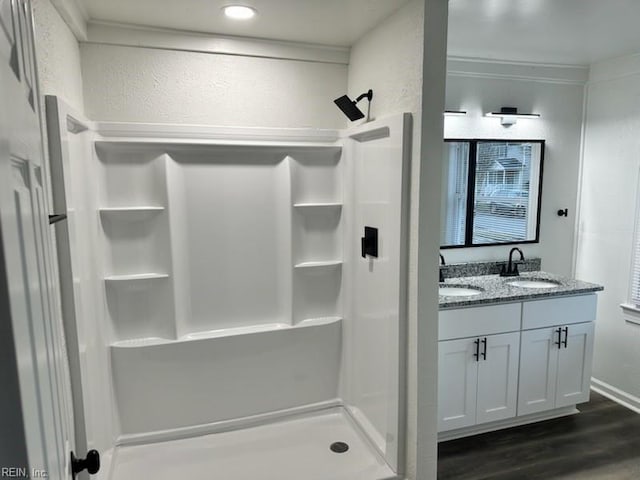 full bath featuring wood finished floors, a sink, a shower stall, double vanity, and crown molding