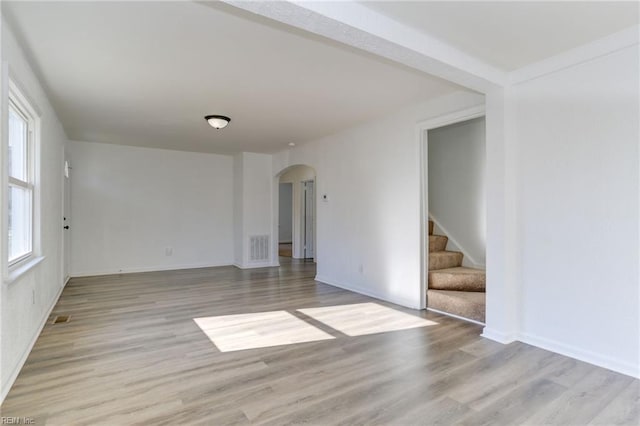 spare room with light wood-style floors, visible vents, stairs, and arched walkways