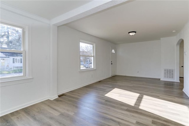 spare room featuring arched walkways, visible vents, baseboards, and wood finished floors