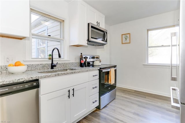 kitchen with light stone countertops, white cabinetry, appliances with stainless steel finishes, and a sink