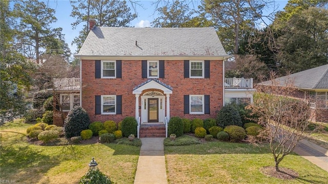 view of front of property with a front yard, a balcony, a chimney, and brick siding