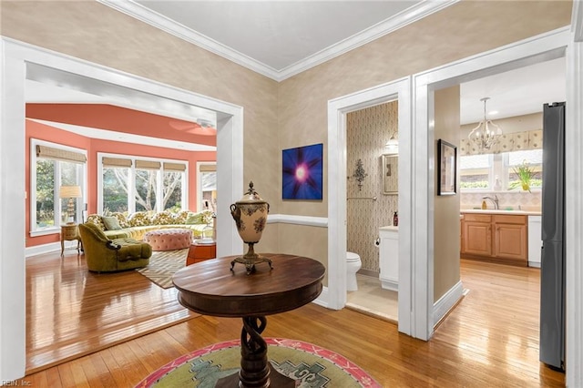 living area featuring an inviting chandelier, baseboards, light wood finished floors, and ornamental molding