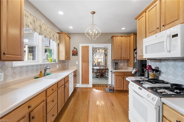 kitchen with a sink, white appliances, light wood-style floors, light countertops, and a chandelier