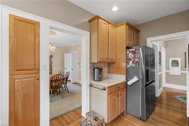 kitchen featuring stainless steel fridge with ice dispenser, light countertops, light wood-type flooring, decorative backsplash, and a notable chandelier