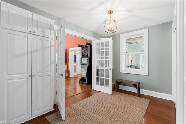 interior space with french doors, baseboards, a notable chandelier, and dark wood-style flooring