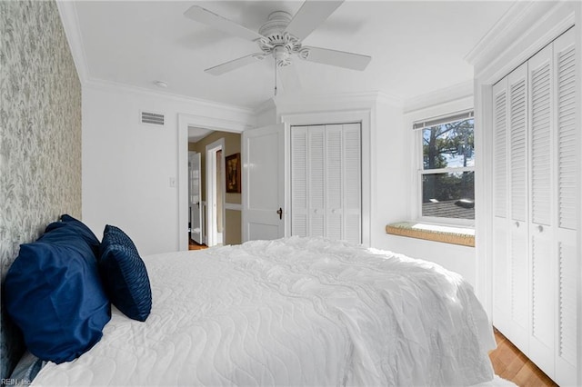 bedroom featuring visible vents, crown molding, multiple closets, and wood finished floors