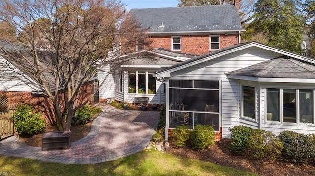 back of house featuring a patio, fence, brick siding, and a sunroom