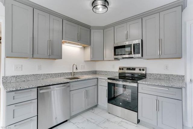 kitchen featuring gray cabinetry, stainless steel appliances, a sink, marble finish floor, and light stone countertops