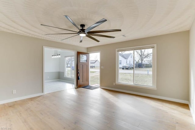 unfurnished room with baseboards, light wood finished floors, and ceiling fan with notable chandelier