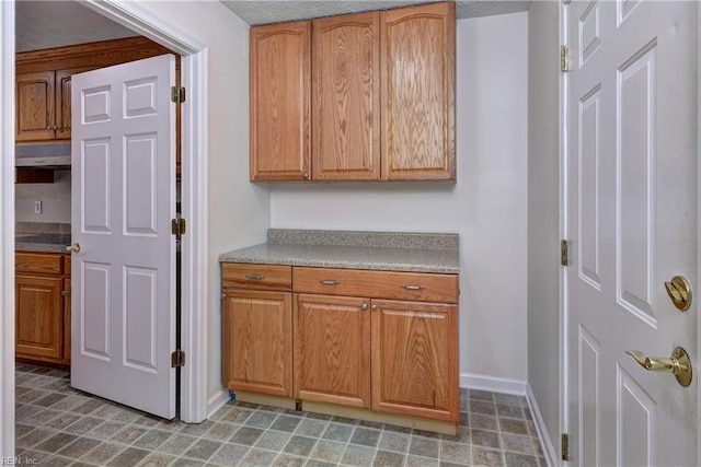 kitchen with light countertops, baseboards, under cabinet range hood, and brown cabinets