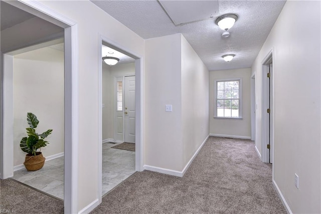 hall with a textured ceiling, baseboards, and carpet floors