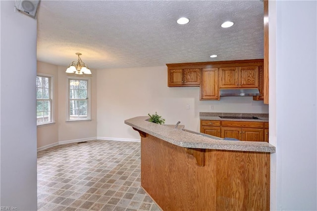 kitchen featuring under cabinet range hood, recessed lighting, brown cabinets, a kitchen breakfast bar, and a sink