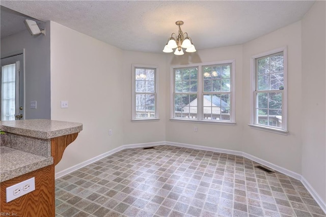 unfurnished dining area featuring a notable chandelier, visible vents, a textured ceiling, and baseboards