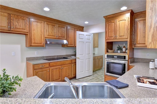 kitchen with a sink, light countertops, under cabinet range hood, stainless steel oven, and black electric cooktop