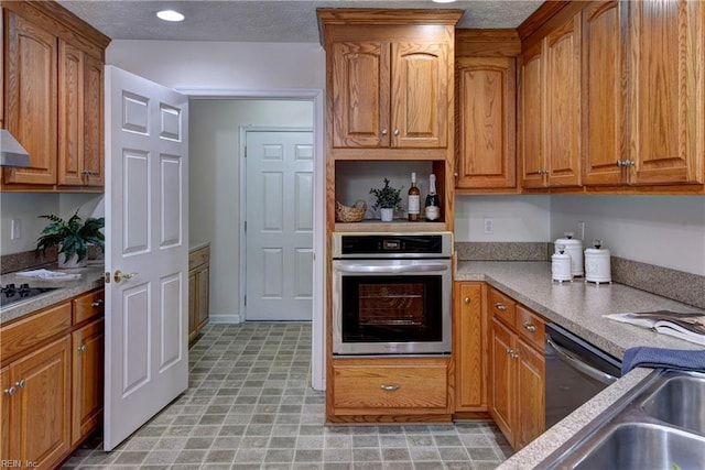 kitchen with ventilation hood, a textured ceiling, appliances with stainless steel finishes, and brown cabinetry