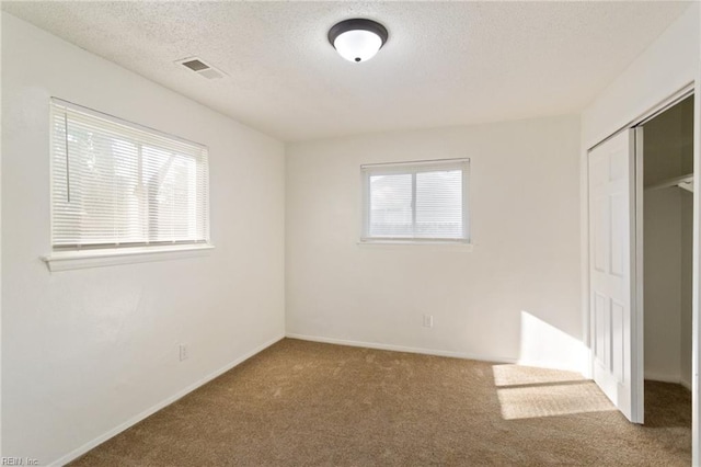 unfurnished bedroom featuring baseboards, visible vents, carpet, a textured ceiling, and a closet