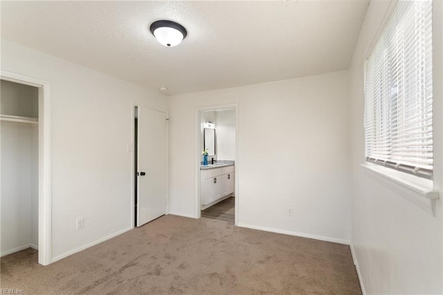 unfurnished bedroom featuring light carpet, a textured ceiling, connected bathroom, and baseboards