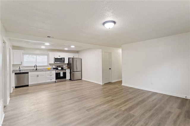 kitchen with open floor plan, stainless steel appliances, light wood-type flooring, white cabinetry, and a sink