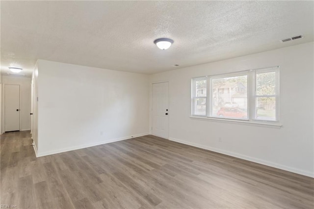 empty room with baseboards, a textured ceiling, visible vents, and wood finished floors