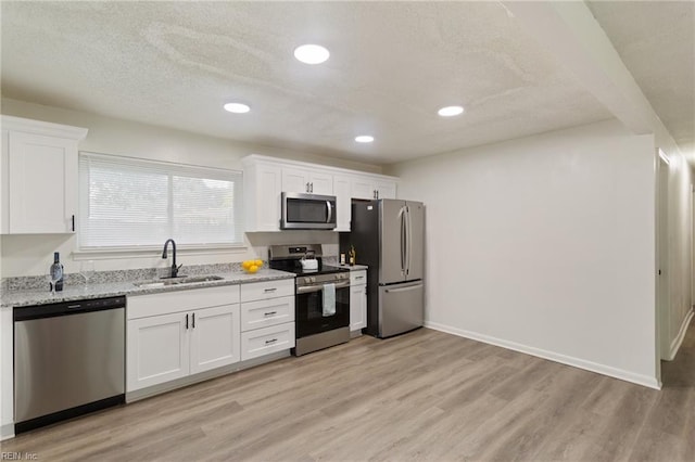 kitchen with stainless steel appliances, a sink, light wood-style flooring, and white cabinetry