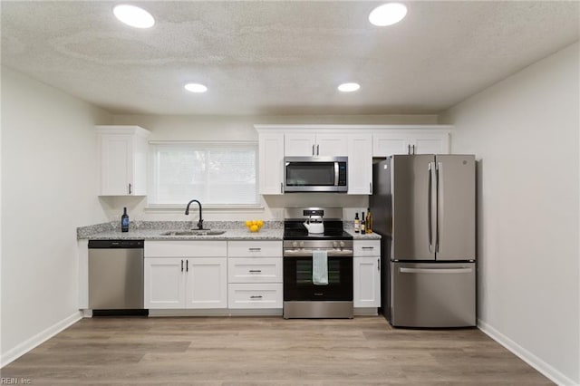 kitchen with stainless steel appliances, white cabinets, a sink, and light wood-style flooring