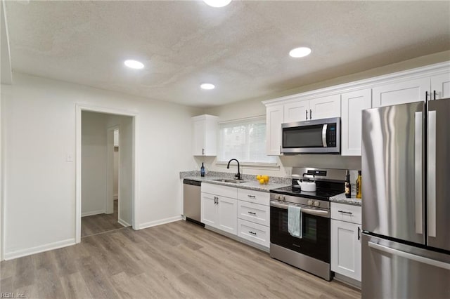 kitchen with stainless steel appliances, a sink, light wood-style flooring, and white cabinets