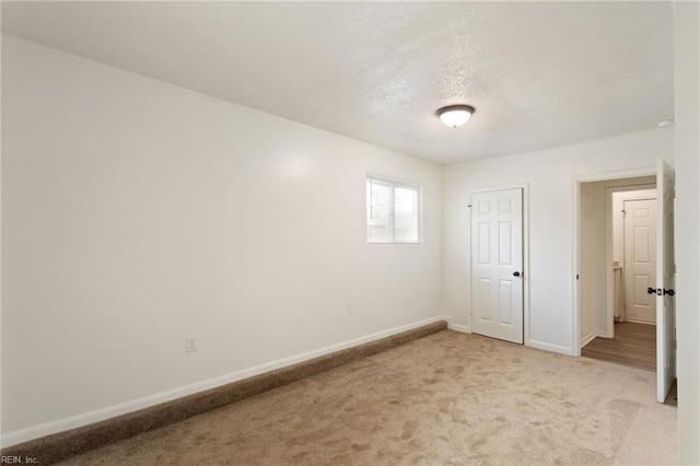 unfurnished room with light carpet, baseboards, and a textured ceiling