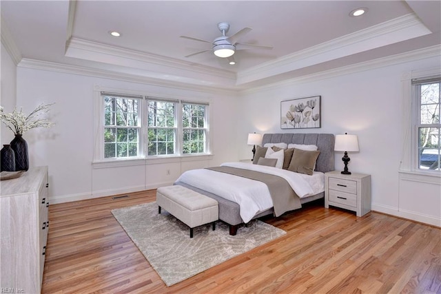 bedroom with baseboards, light wood-type flooring, and a tray ceiling