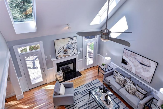 living area featuring a fireplace, lofted ceiling with skylight, wood finished floors, and a wainscoted wall