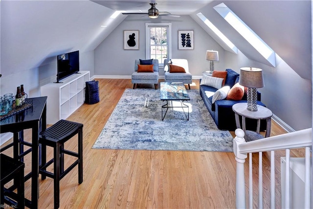 living area with ceiling fan, baseboards, vaulted ceiling with skylight, and wood finished floors