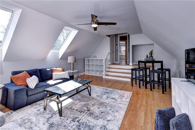 living area featuring stairway, vaulted ceiling with skylight, wood finished floors, and ceiling fan