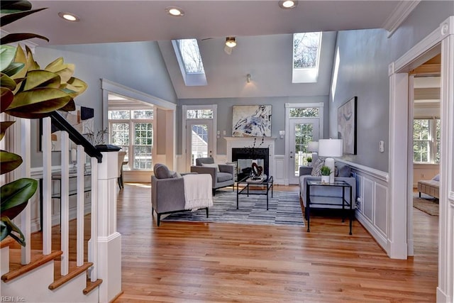 living room featuring stairway, a wainscoted wall, light wood finished floors, a fireplace, and lofted ceiling with skylight