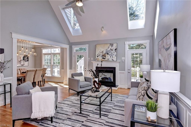 living area with a wainscoted wall, a skylight, a high end fireplace, and light wood finished floors