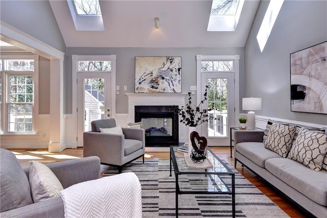 living area with a wealth of natural light, a wainscoted wall, a skylight, and wood finished floors