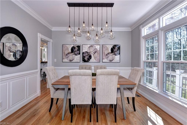 dining room featuring light wood finished floors, a wainscoted wall, a decorative wall, and crown molding