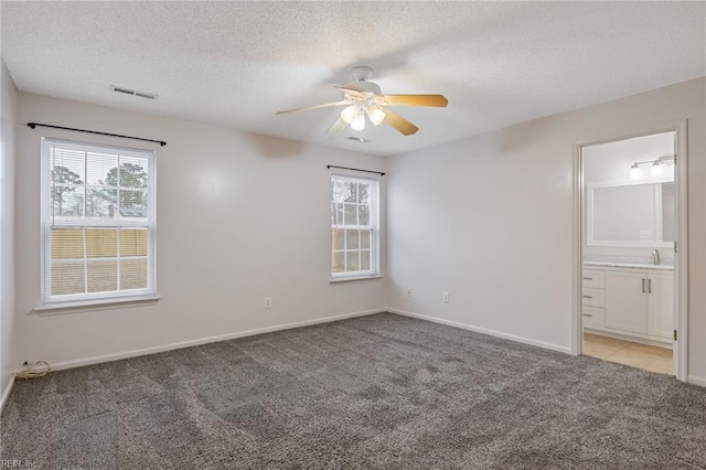 spare room featuring a textured ceiling, a healthy amount of sunlight, visible vents, and light colored carpet